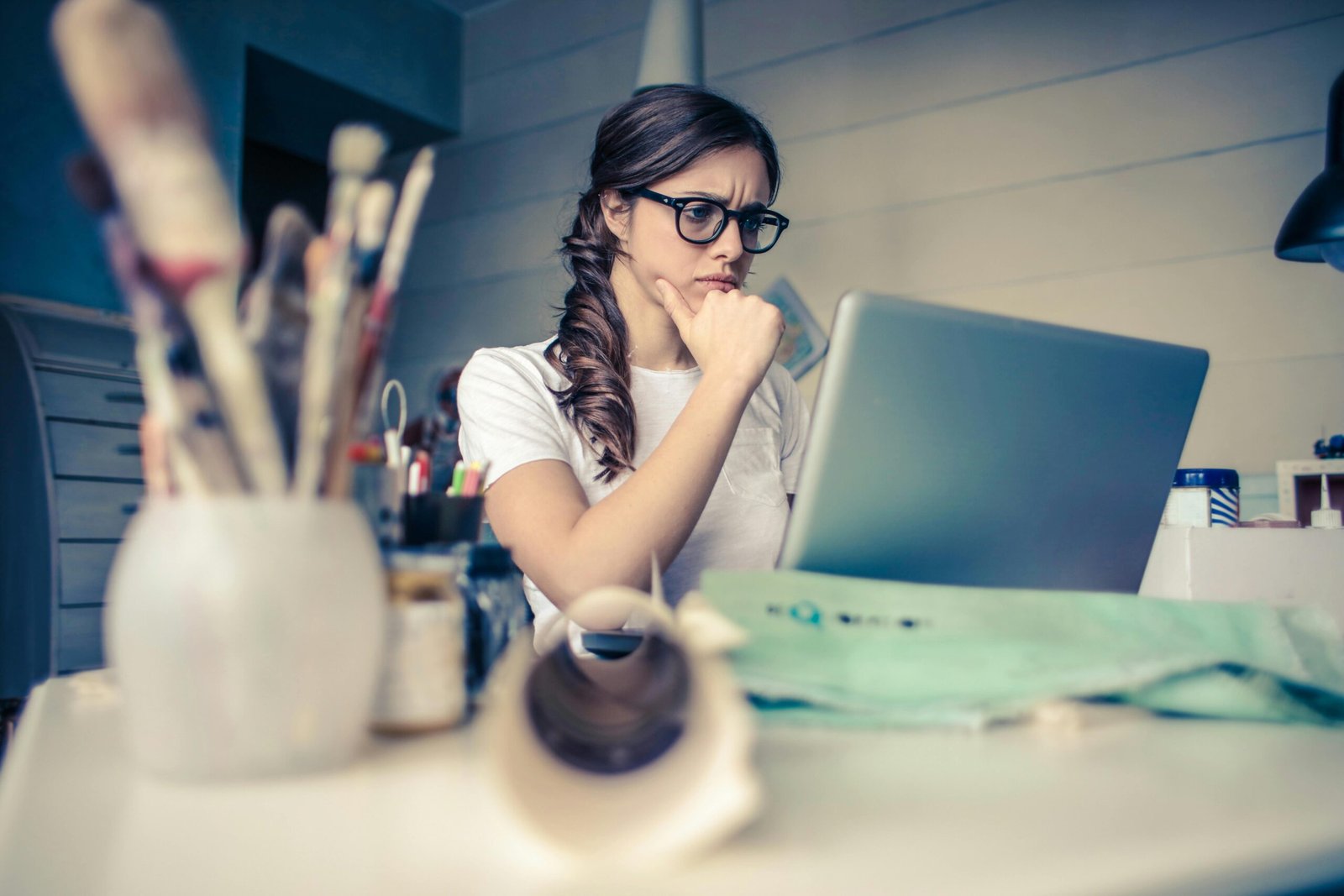 women is experiencing creative blocks staring at a computer with paintbrushes in the foreground.